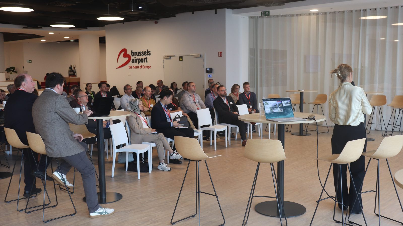 Delegates seated in the conference room at Brussels Airport, under the Brussels Airport logo, during a presentation