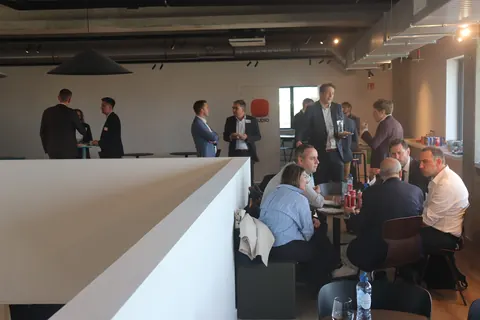 Delegates talking in small groups and seated at tables in a bright lounge at AHLEX