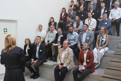 Around forty delegates seated on tiered steps listening to a speaker standing in the foreground