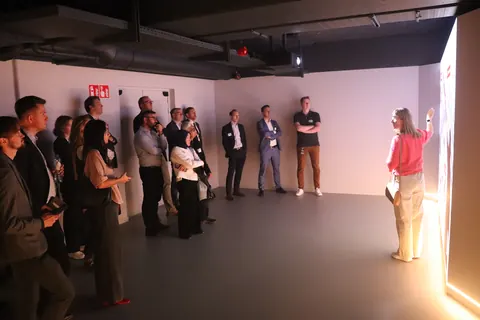 Delegates standing in a studio space while a guide points to a large illuminated wall display