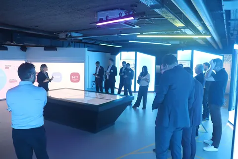 Delegates in a training room lit in blue, around an interactive table with wall-sized screens