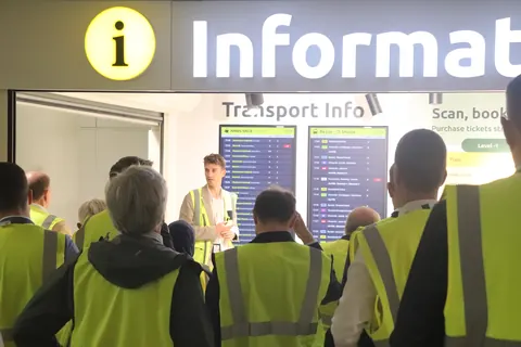 Delegates in high-visibility vests gathered at the Transport Info desk in Brussels Airport, under train departure screens