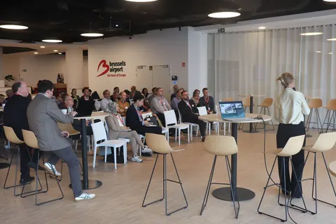 A speaker standing at a high table addresses delegates in the conference room at Brussels Airport