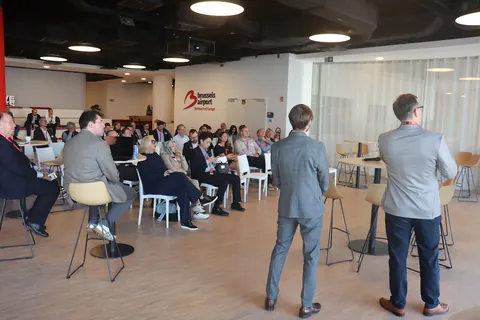 Two speakers stand facing delegates seated in the conference room