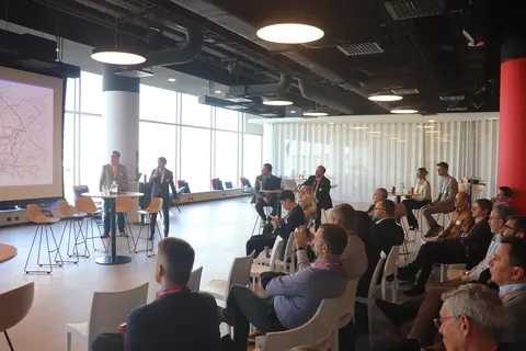 Delegates seated by the windows watch a speaker at the front, beside a projected map