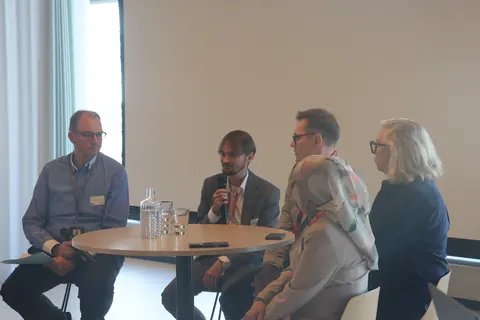 Four panellists seated around a high table, one speaking into a microphone